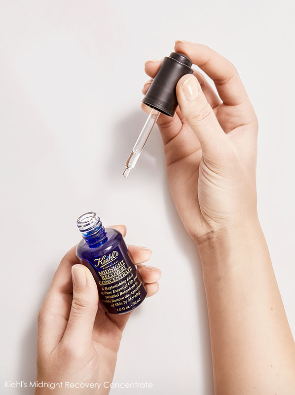 Pair of hands holding an open bottle of Kiehl's Midnight Recovery Concentrate